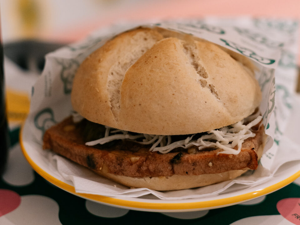 Ein Sandwich mit geriebenem Käse und einer Scheibe Fleisch in einem runden Brötchen auf einem Teller.