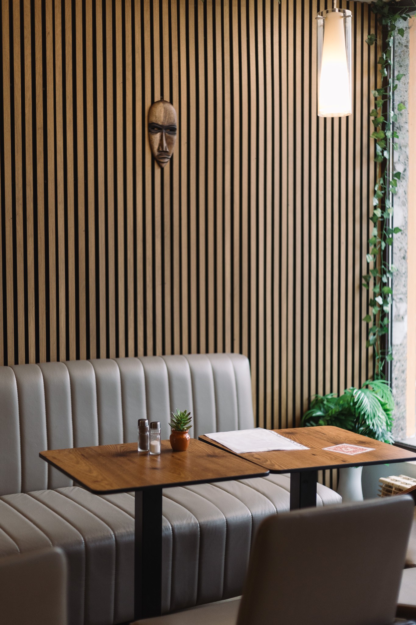 Modernes Café mit beigen Sitzgelegenheiten, einem Holztisch, einer Wandmaske und einer Hängelampe.