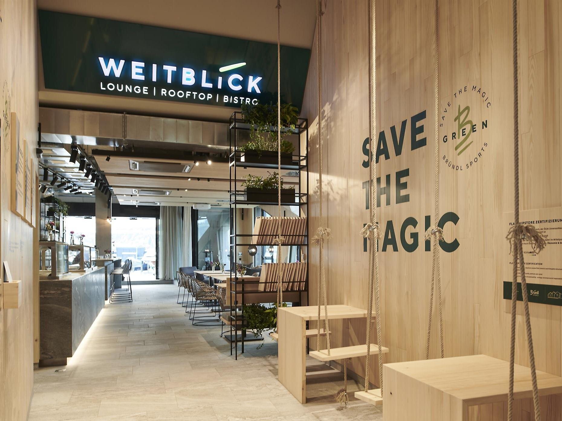 Modernes Café mit Holzdekor, hängenden Schaukeln und sichtbaren Schildern SAVE THE MAGIC und WEITBLICK.