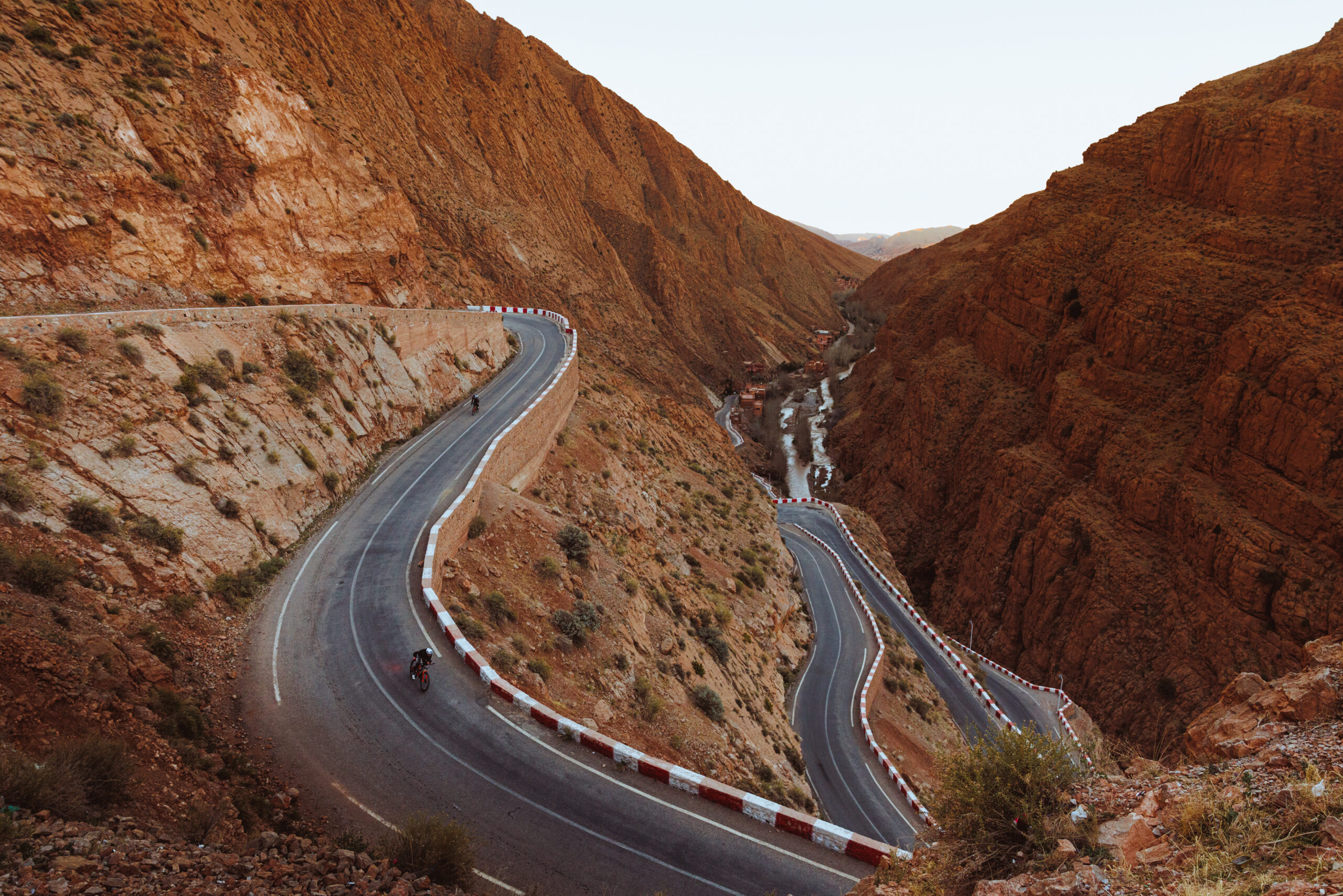 Eine kurvenreiche Bergstraße mit scharfen Kurven führt durch eine felsige, rötliche Schlucht.