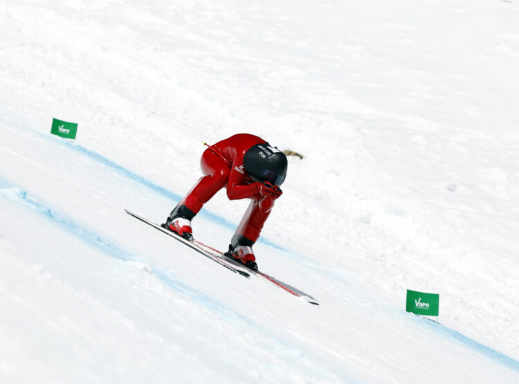 Ein Skifahrer im roten Anzug hockt tief, während er auf einer verschneiten Piste bergab fährt.