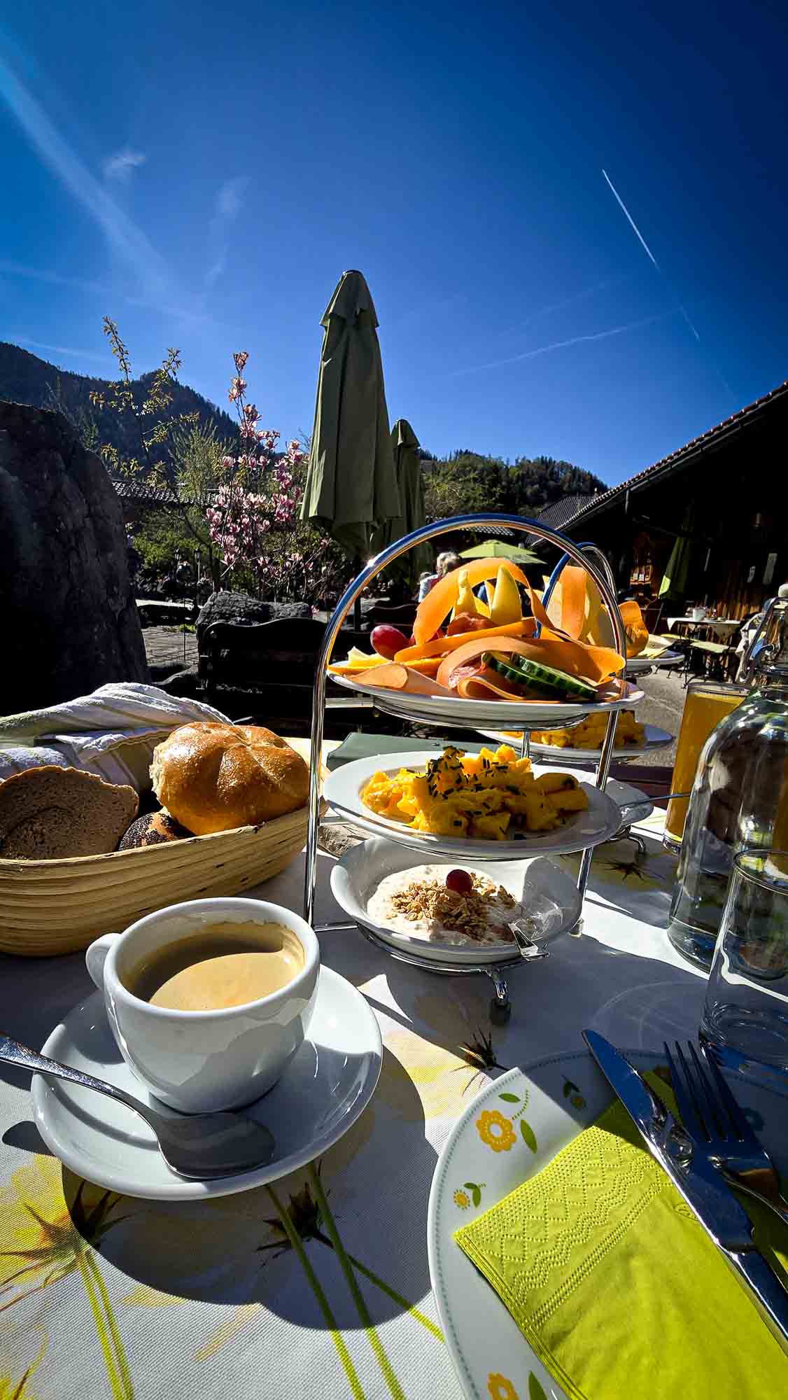 Fr&uuml;hst&uuml;ckstisch im Freien in Kathis Blumencaf&eacute; mit Kaffee, Geb&auml;ck, Obst, Eiern und Bergblick.