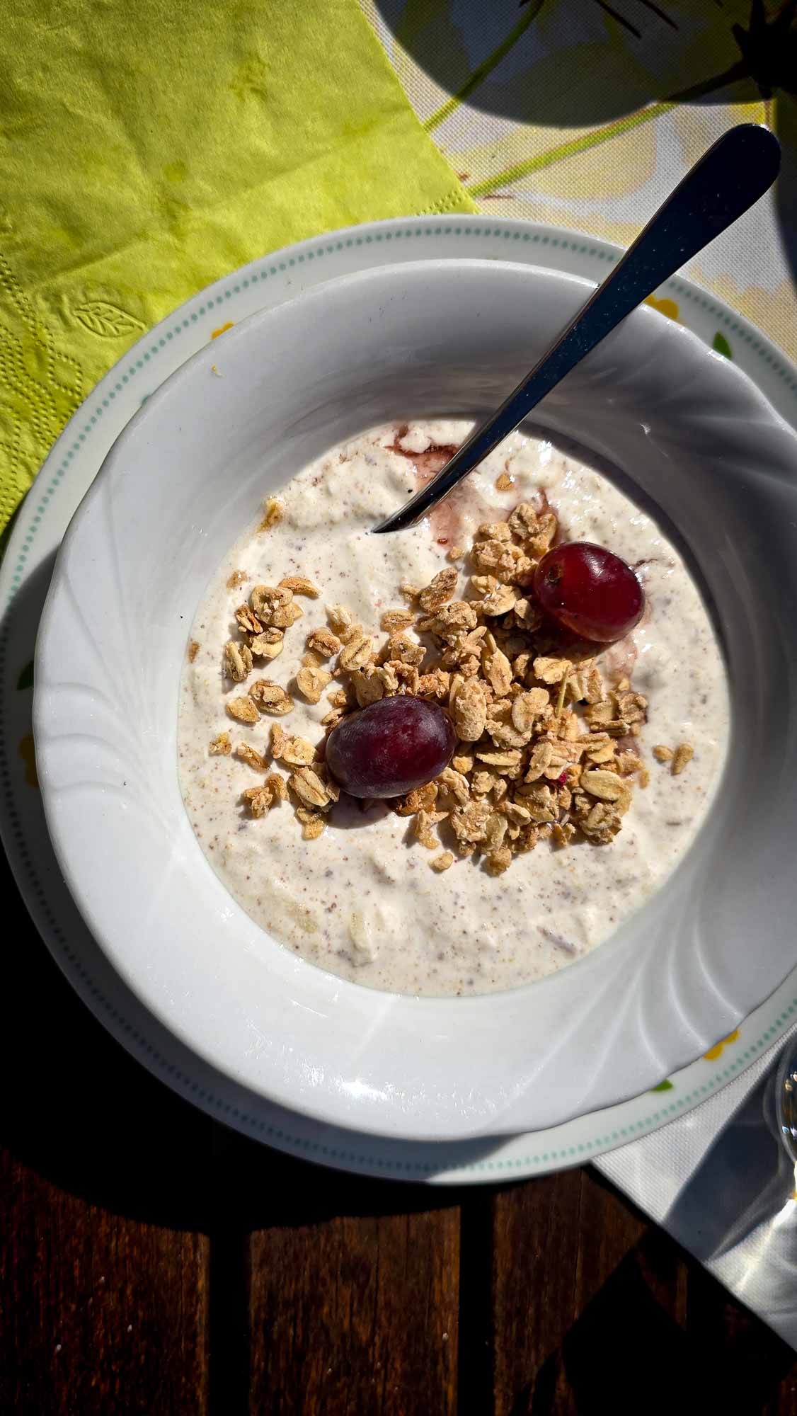 Eine Schale M&uuml;sli mit M&uuml;sli und Trauben in Kathis Blumencaf&eacute;, serviert mit einem L&ouml;ffel auf einem Holztisch.