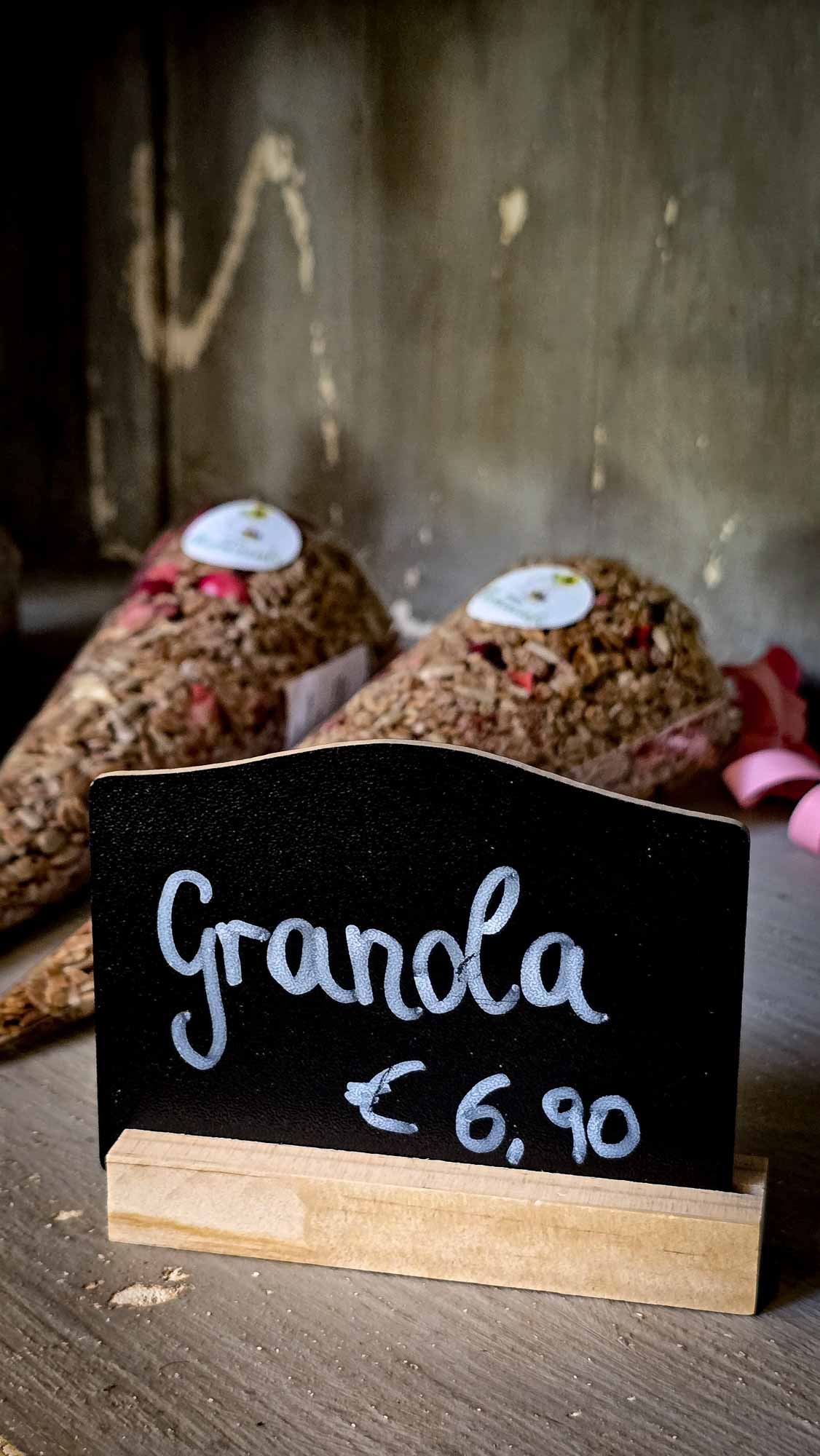 M&uuml;slit&uuml;ten in Kathis Blumencaf&eacute; hinter einem Kreideschild mit der Aufschrift Granola 6,90 &euro; auf einem Holzregal.