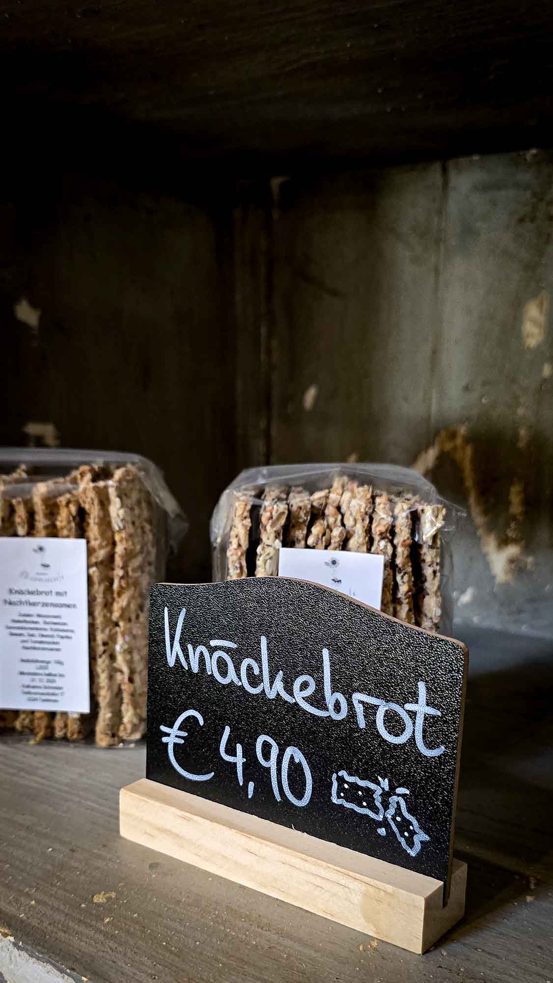 Kn&auml;ckebrotpackungen mit der Aufschrift Kn&auml;ckebrot &euro; 4,90 stehen in Kathis Blumencaf&eacute; in einem Holzregal.