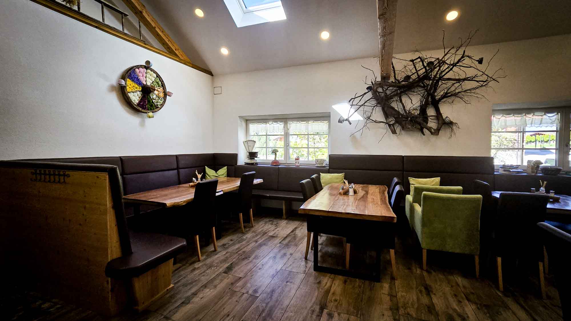 Gem&uuml;tliches Kathis Blumencaf&eacute; mit Holztischen, gepolsterten Sitzgelegenheiten, Wandkunst und nat&uuml;rlichem Licht durch Oberlicht und Fenster.