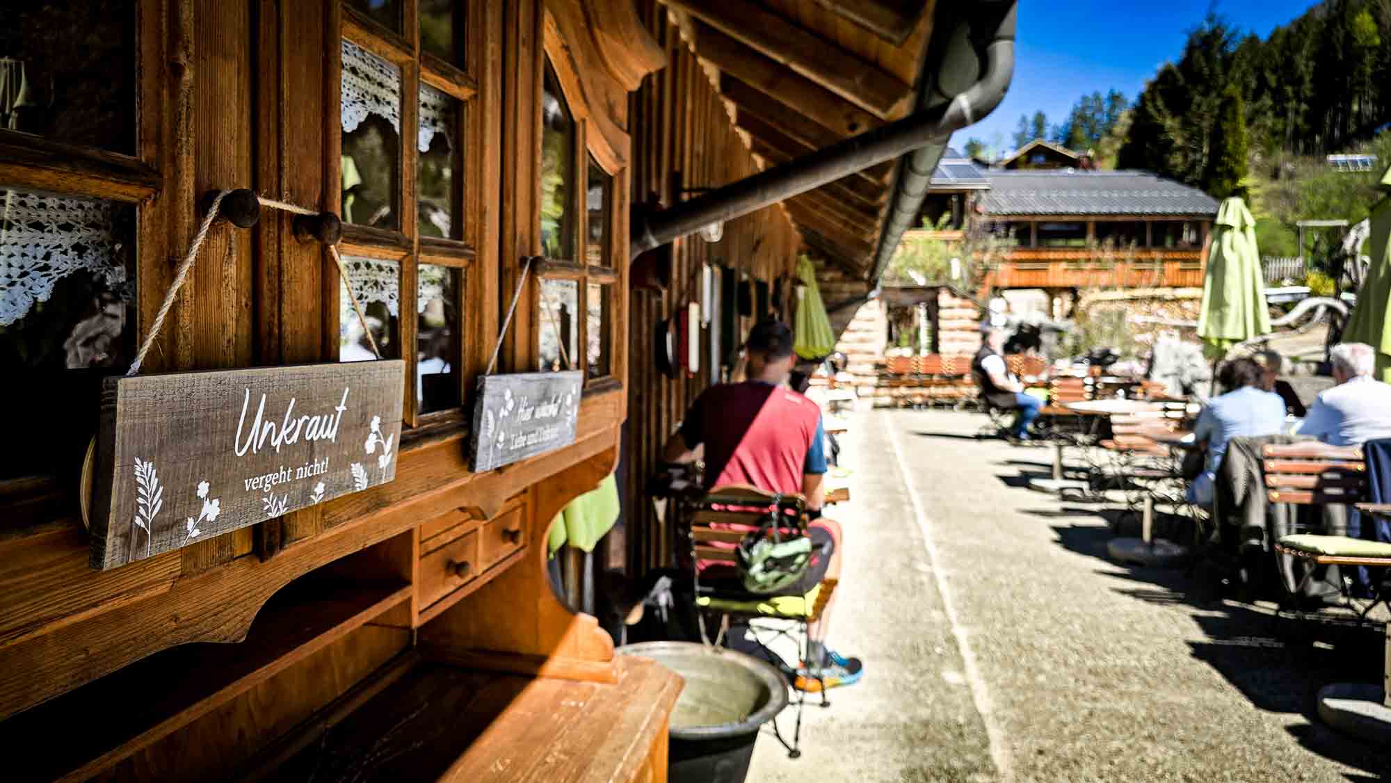 Außencafé mit Holzdekor in Kathis Blumencafé, Menschen genießen die Aussicht an einem sonnigen Tag. © Melanie Deisl