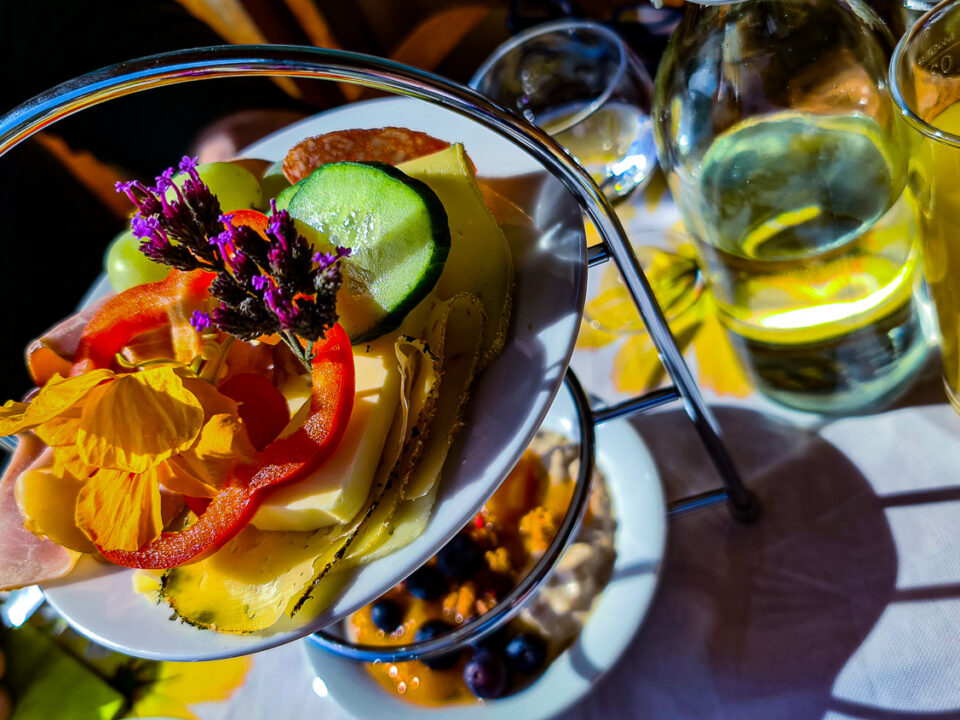 Ein Teller mit geschnittenem Gemüse, Käse und Blumen in Kathis Blumencafé neben einem Glas Orangensaft.