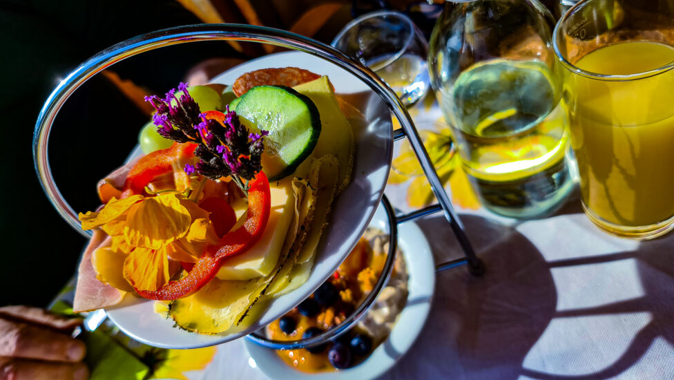 Ein Teller mit geschnittenem Gemüse, Käse und Blumen in Kathis Blumencafé neben einem Glas Orangensaft.