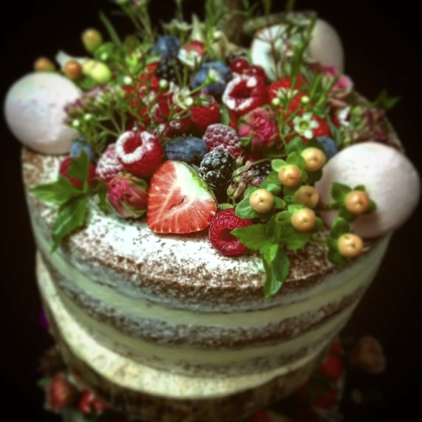 Ein nackter Kuchen von Kathis Blumencaf&eacute; mit Beeren, Macarons, Minzbl&auml;ttern und Puderzucker belegt.