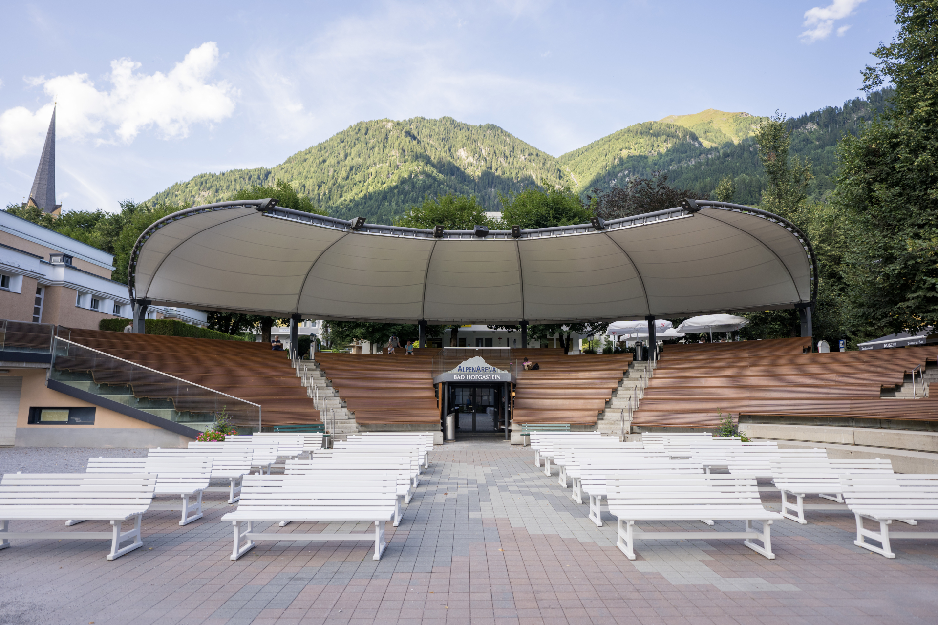 Amphitheater im Freien mit wei&szlig;en B&auml;nken und einem Baldachin vor dem Hintergrund gr&uuml;ner Berge und blauen Himmels.