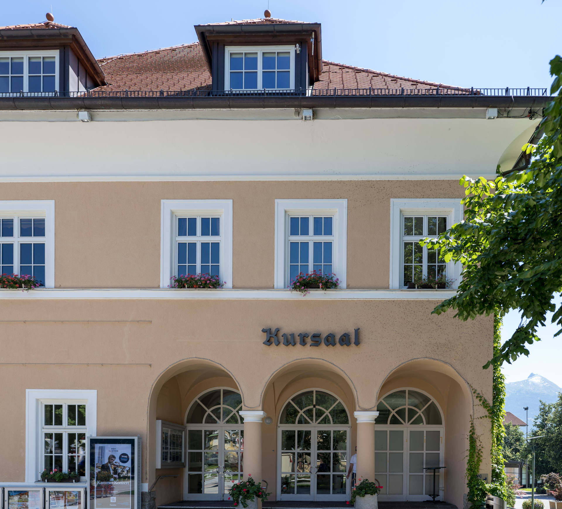 Cremefarbenes Geb&auml;ude mit Rundbogenfenstern und Kursaal-Schild, umgeben von Gr&uuml;nanlagen.
