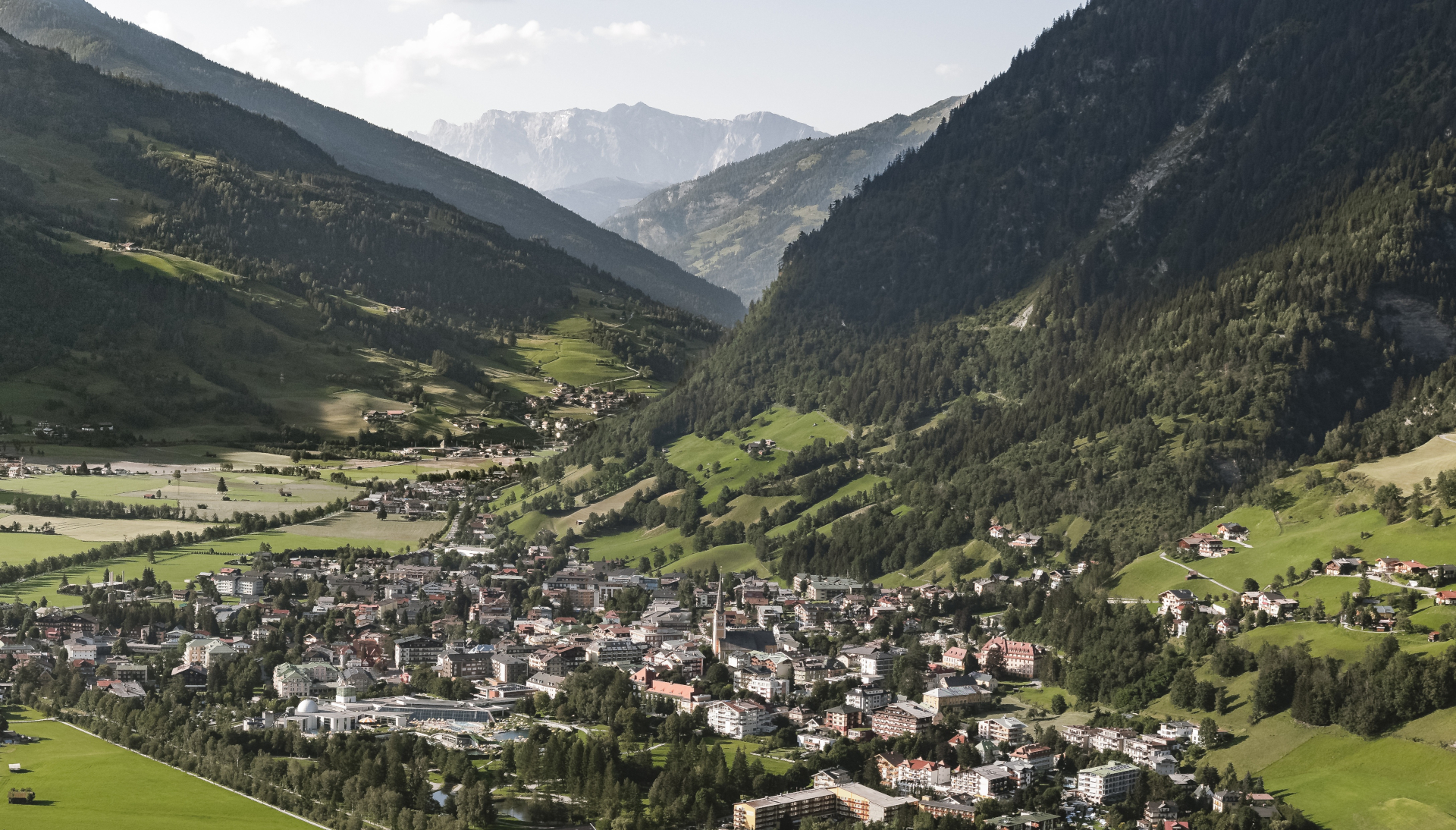 Eine kleine Stadt, eingebettet in ein grünes Tal zwischen bewaldeten Bergen unter einem teilweise bewölkten Himmel.
