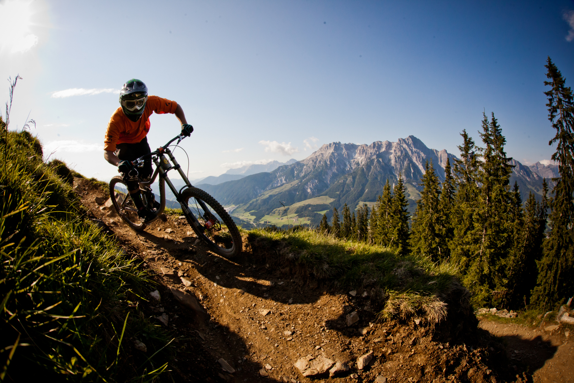 Ein Mountainbiker f&auml;hrt auf einem unbefestigten Weg mit malerischen Bergen und Kiefern im Hintergrund.