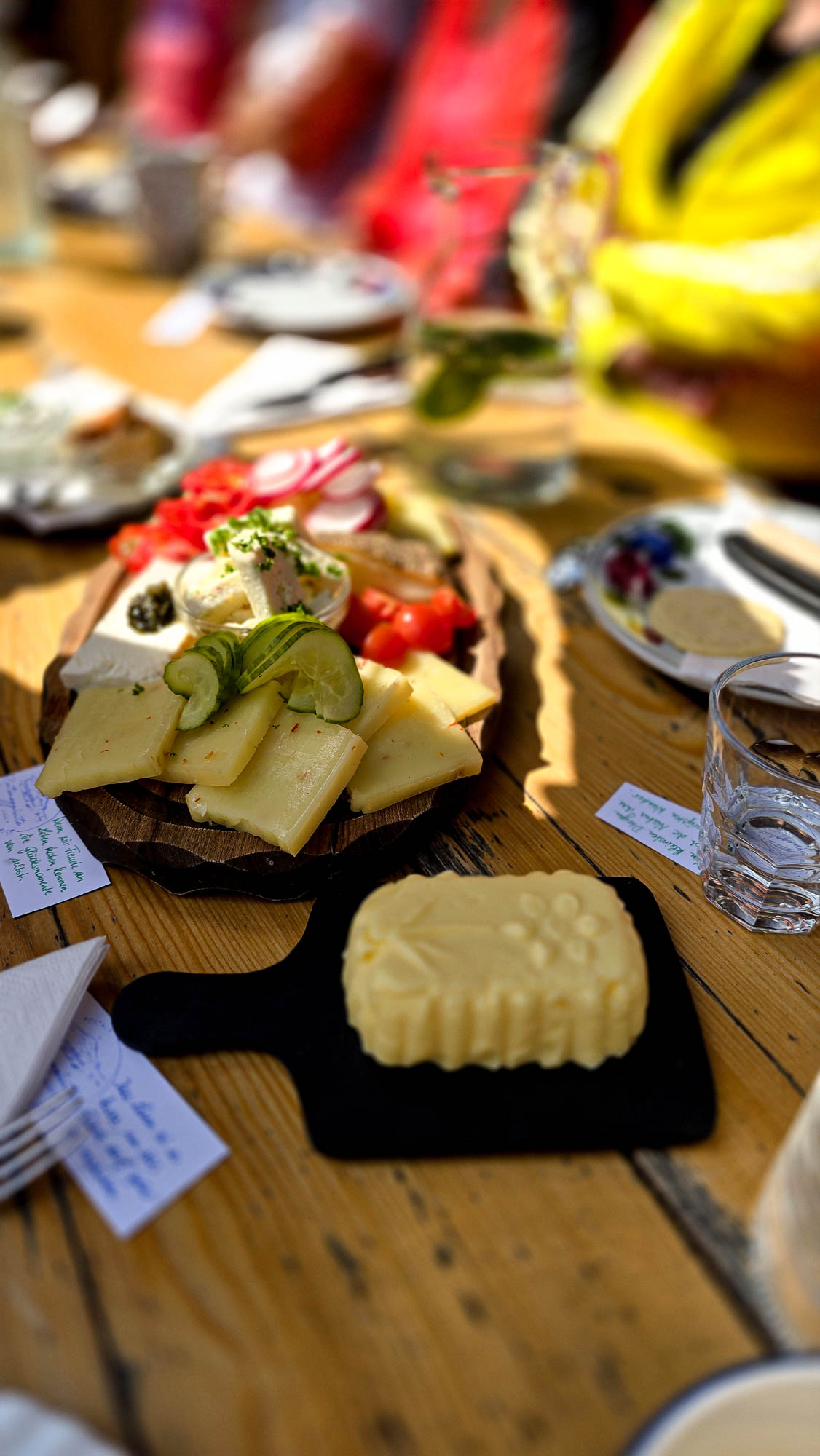Ein Holztisch mit aufgeschnittenem K&auml;se, Gem&uuml;se, geformter Butter und einem vom Yoga inspirierten Gedeck.