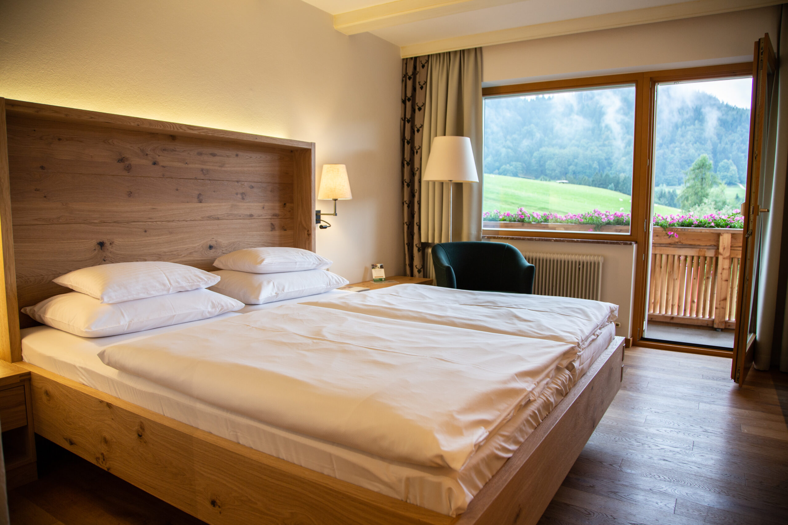 Ein gem&uuml;tliches Hotelzimmer mit einem gro&szlig;en Bett, Holzm&ouml;beln und einem Fenster mit Blick auf gr&uuml;ne H&uuml;gel.
