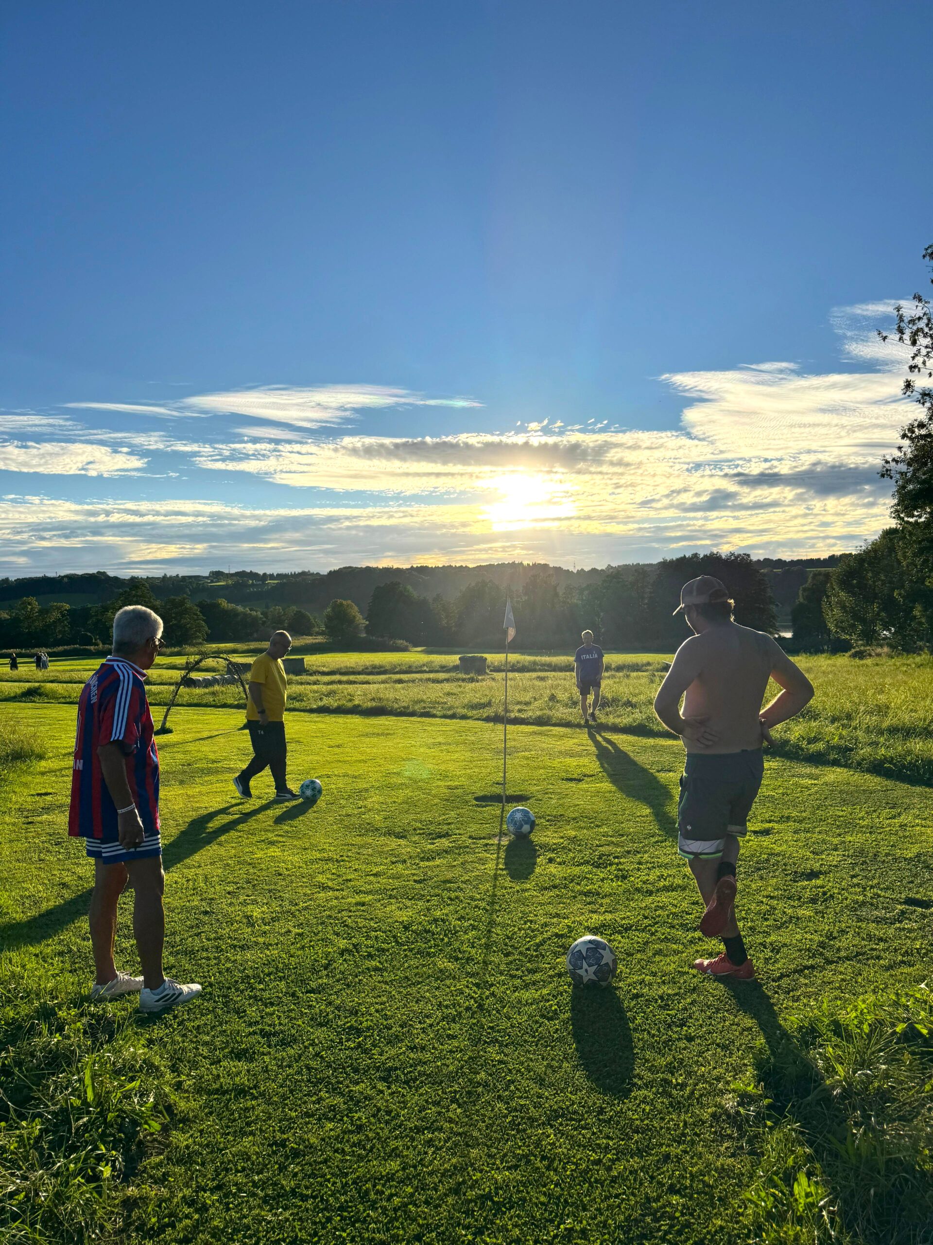 Vier Personen stehen bei Sonnenuntergang mit Fu&szlig;b&auml;llen auf einer Wiese und bereiten sich auf ein Spiel vor.