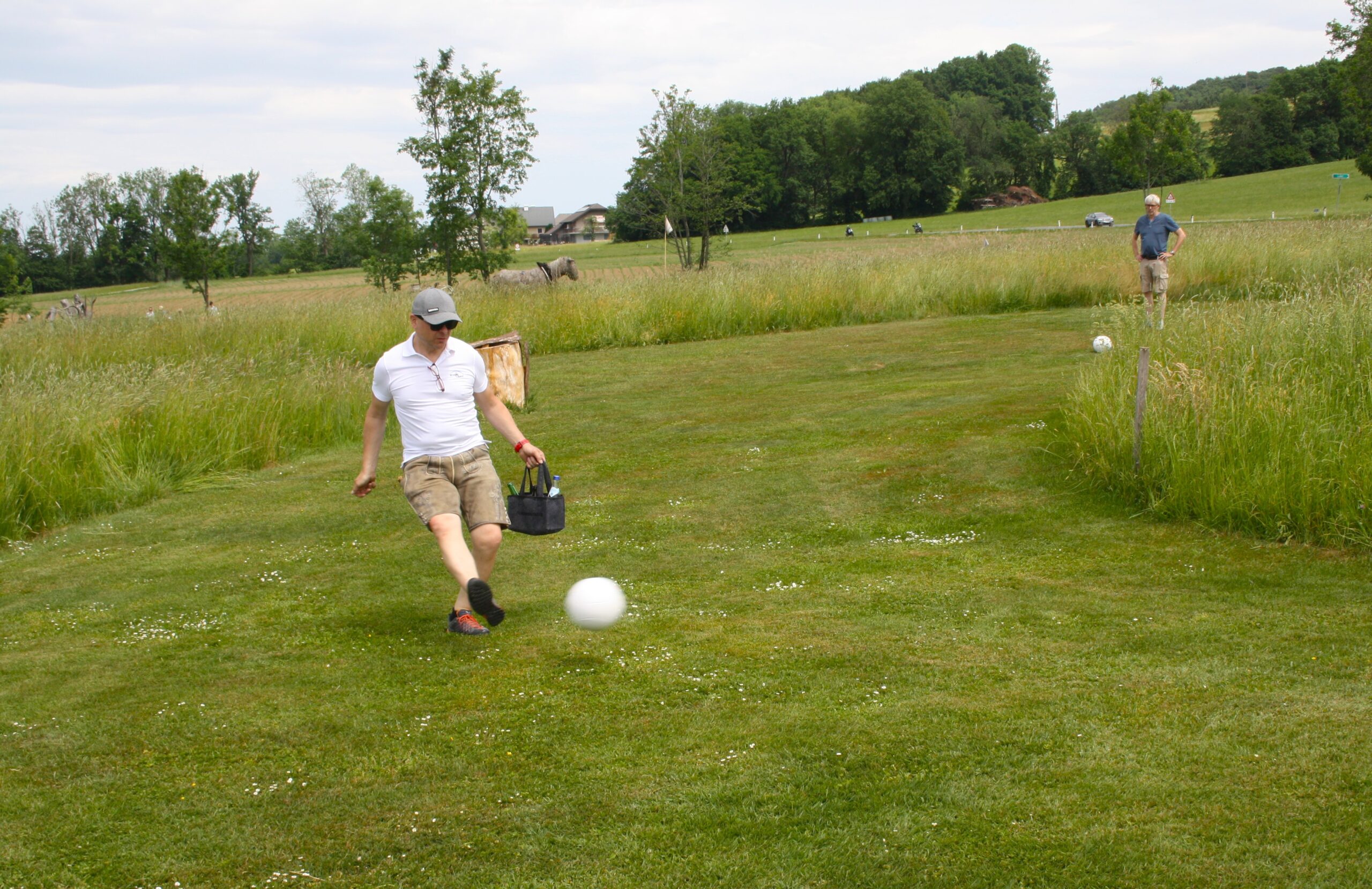Eine Person kickt einen wei&szlig;en Ball auf einer Wiese, w&auml;hrend eine andere Person im Hintergrund steht.
