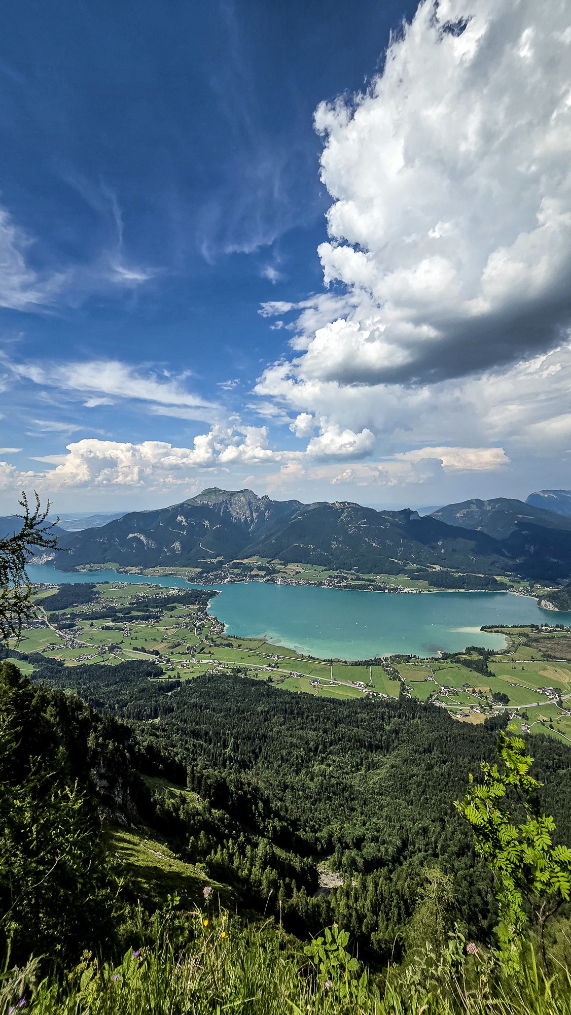 Ein t&uuml;rkisfarbener See in der N&auml;he der Bleckwandh&uuml;tte, umgeben von gr&uuml;nen H&uuml;geln und Bergen unter blauem Himmel.