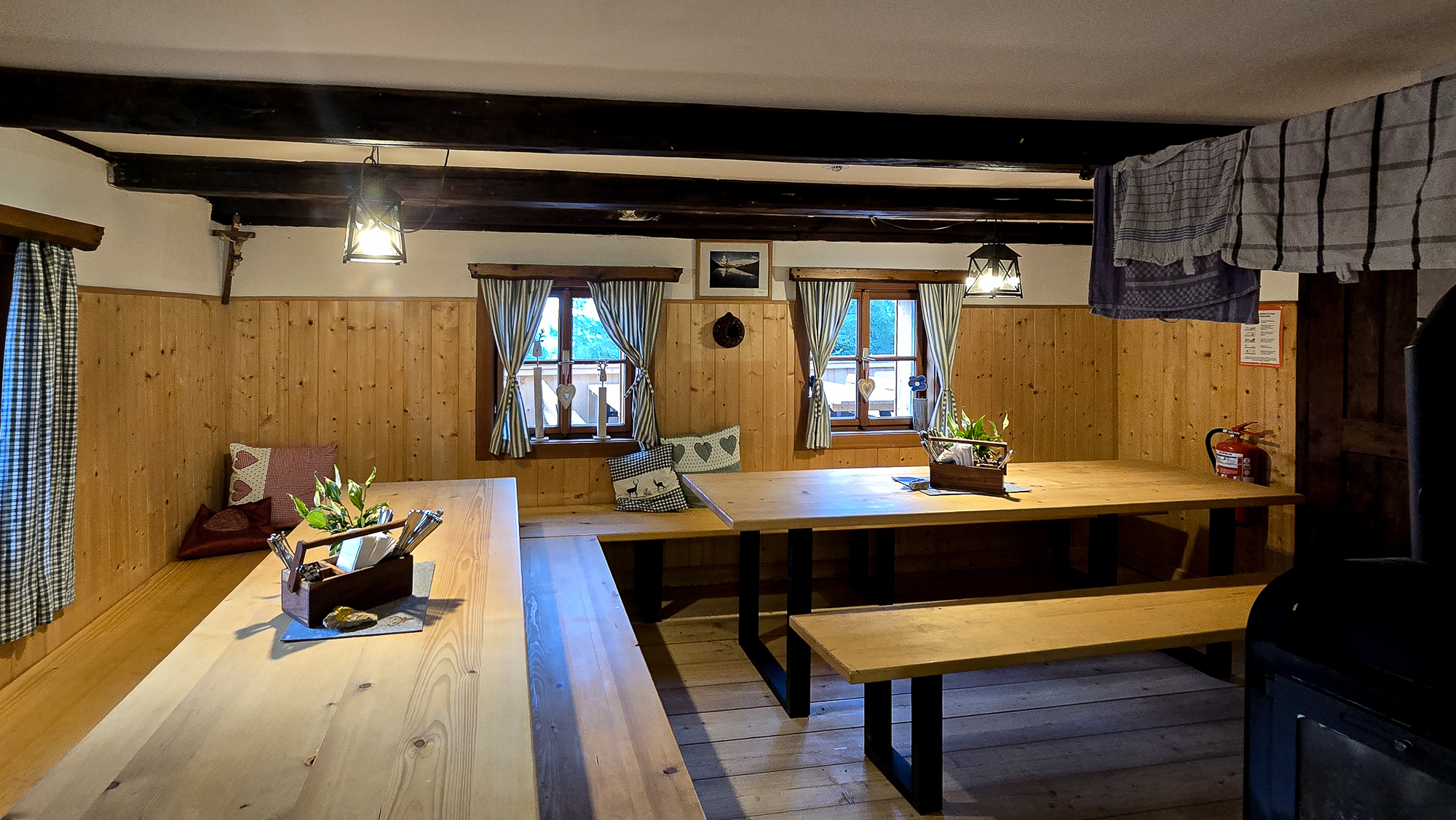 Gem&uuml;tliches Esszimmer aus Holz in der Bleckwandh&uuml;tte mit B&auml;nken, Tischen, Topfpflanzen und sonnendurchfluteten Fenstern mit Vorh&auml;ngen.