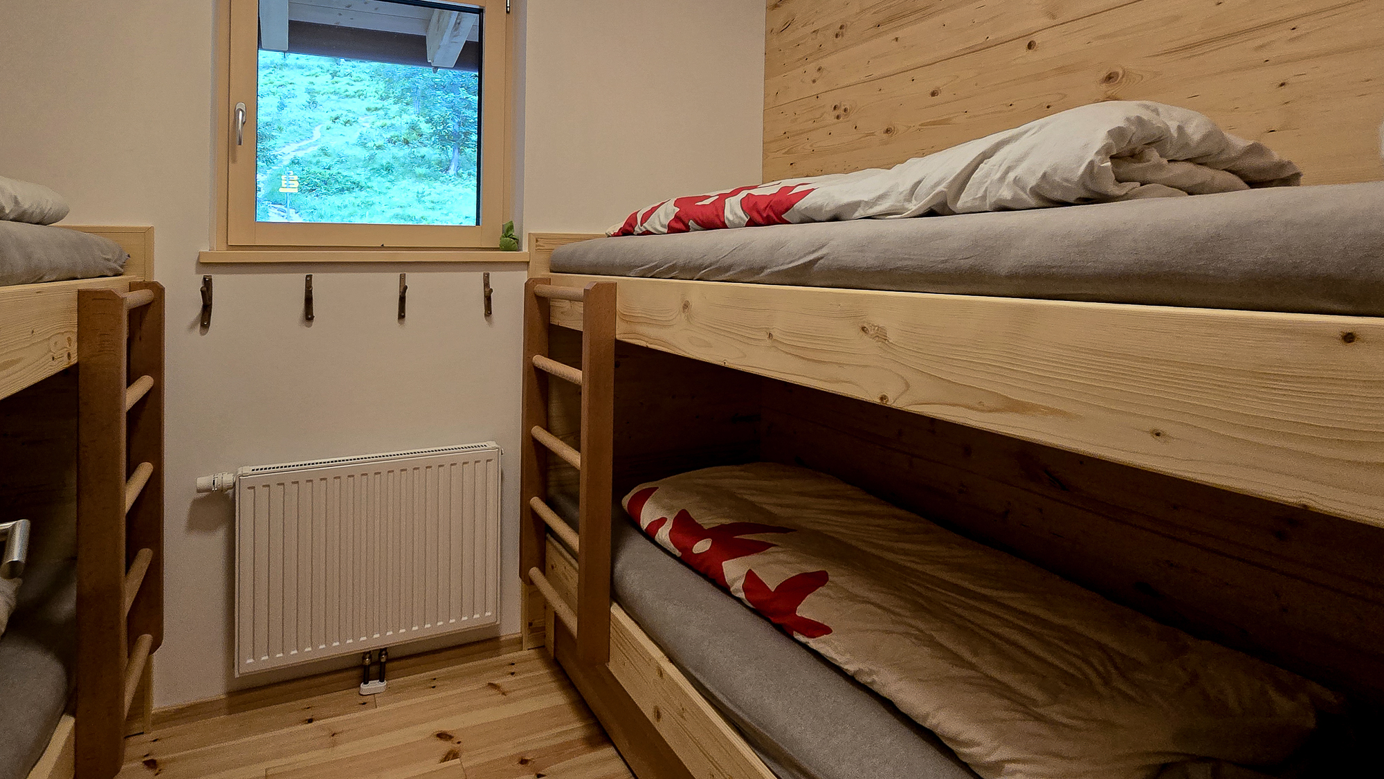 Ein gem&uuml;tliches Zimmer in der Bleckwandh&uuml;tte mit zwei Holz-Etagenbetten, Bettw&auml;sche, einem Fenster und Haken an der Wand.