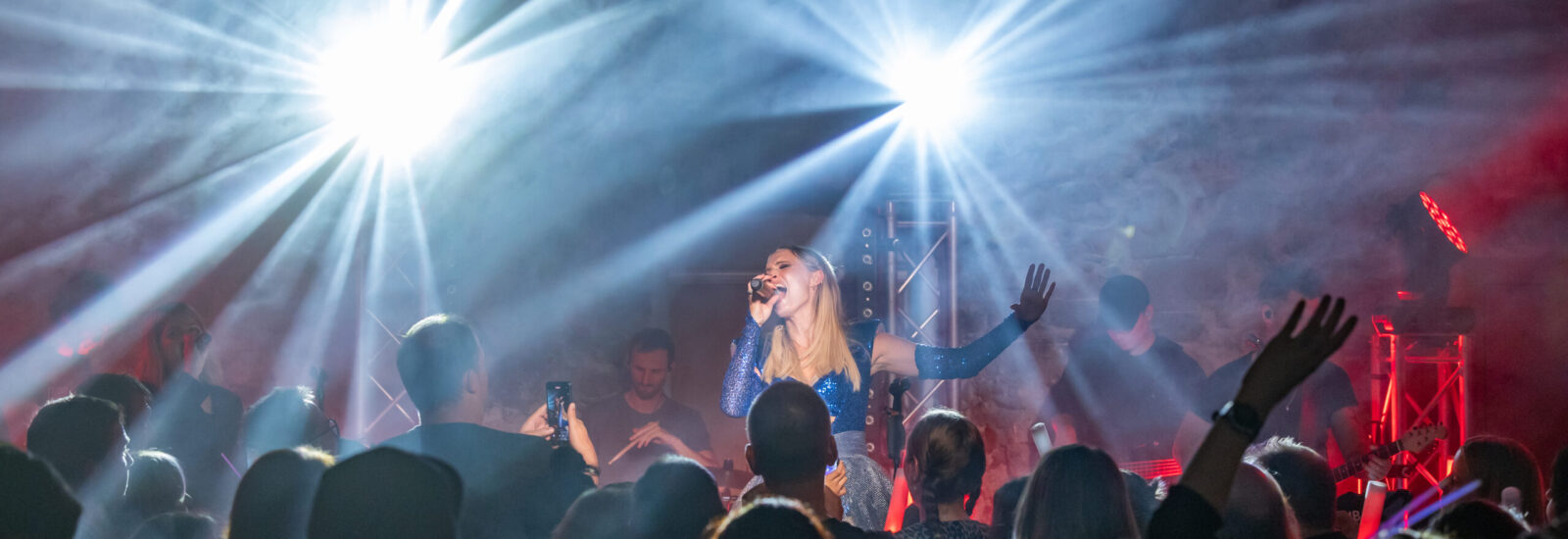 Ein Sänger tritt auf der Bühne auf, während helles Licht auf ihn scheint und das Publikum das Konzert genießt.
