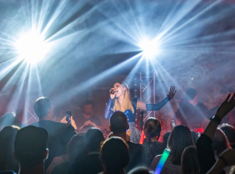 Ein Sänger tritt auf der Bühne auf, während helles Licht auf ihn scheint und das Publikum das Konzert genießt.
