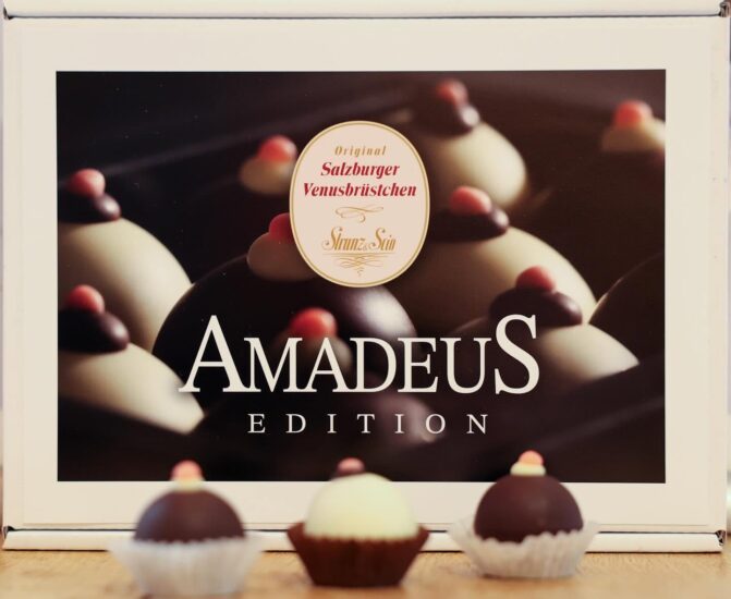 Schachtel mit der Aufschrift „Amadeus Edition“, in der sich Pralinen befinden, und drei verschiedenen Pralinen davor.