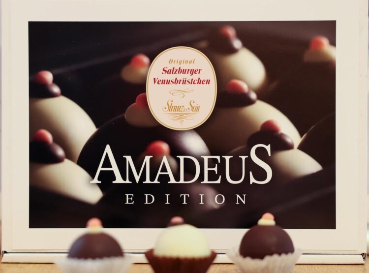 Schachtel mit der Aufschrift „Amadeus Edition“, in der sich Pralinen befinden, und drei verschiedenen Pralinen davor.