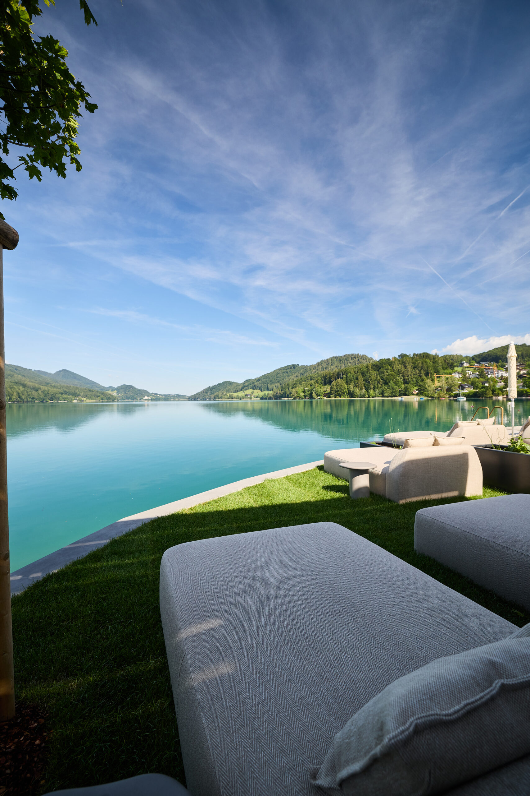 Von den Liegest&uuml;hlen aus hat man einen Blick auf einen ruhigen See mit klarem, blauem Wasser und &uuml;ppig gr&uuml;nen H&uuml;geln unter einem strahlend blauen Himmel.