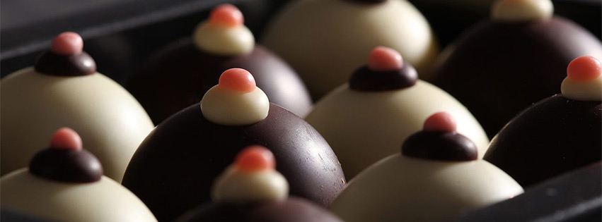 Reihen runder Pralinen mit weißer und dunkler Glasur, jeweils mit Sahne und einem kleinen rosa Punkt verziert.