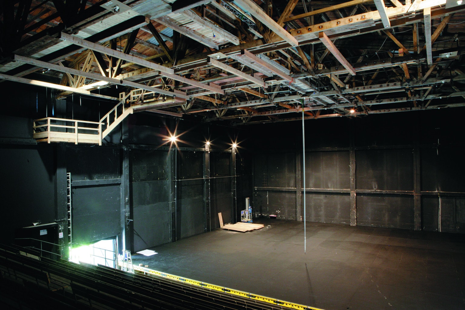 Ein gro&szlig;er, leerer Black-Box-Theaterraum mit freiliegenden Balken, hoher Decke und einer Empore auf der linken Seite der B&uuml;hne.