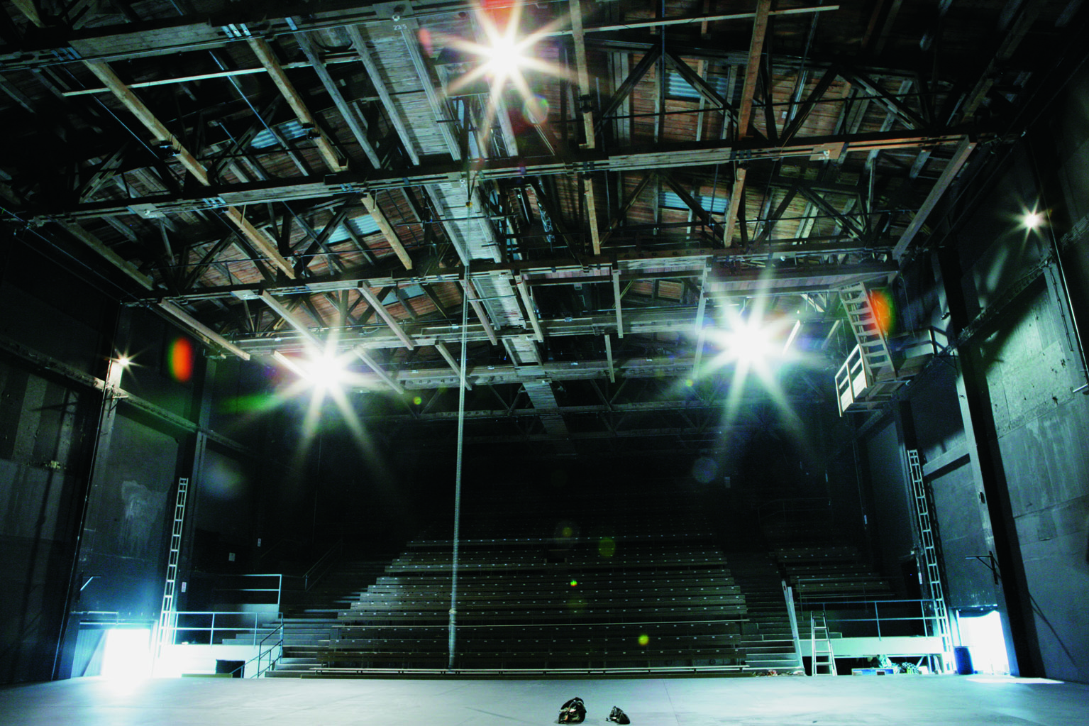 Ein leeres Theater, in dem helles B&uuml;hnenlicht auf die Holzbalken der Decke und die leeren Sitzreihen f&auml;llt.