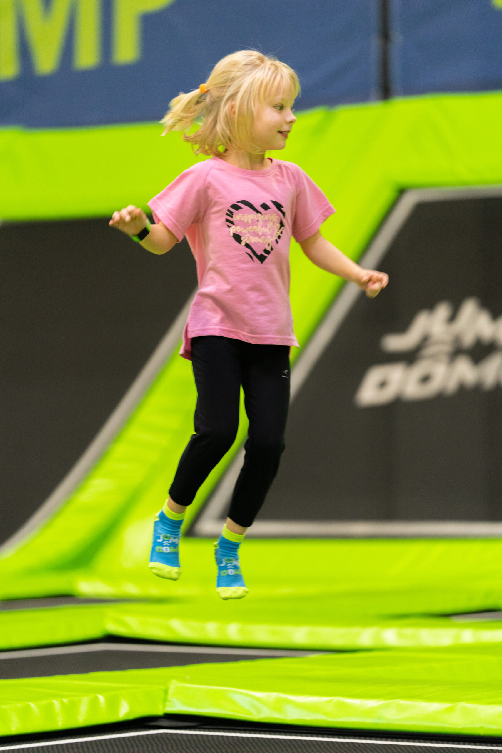 Ein kleines Kind in einem rosa Hemd und blauen Socken springt in einem Indoor-Spielzentrum auf einem Trampolin.