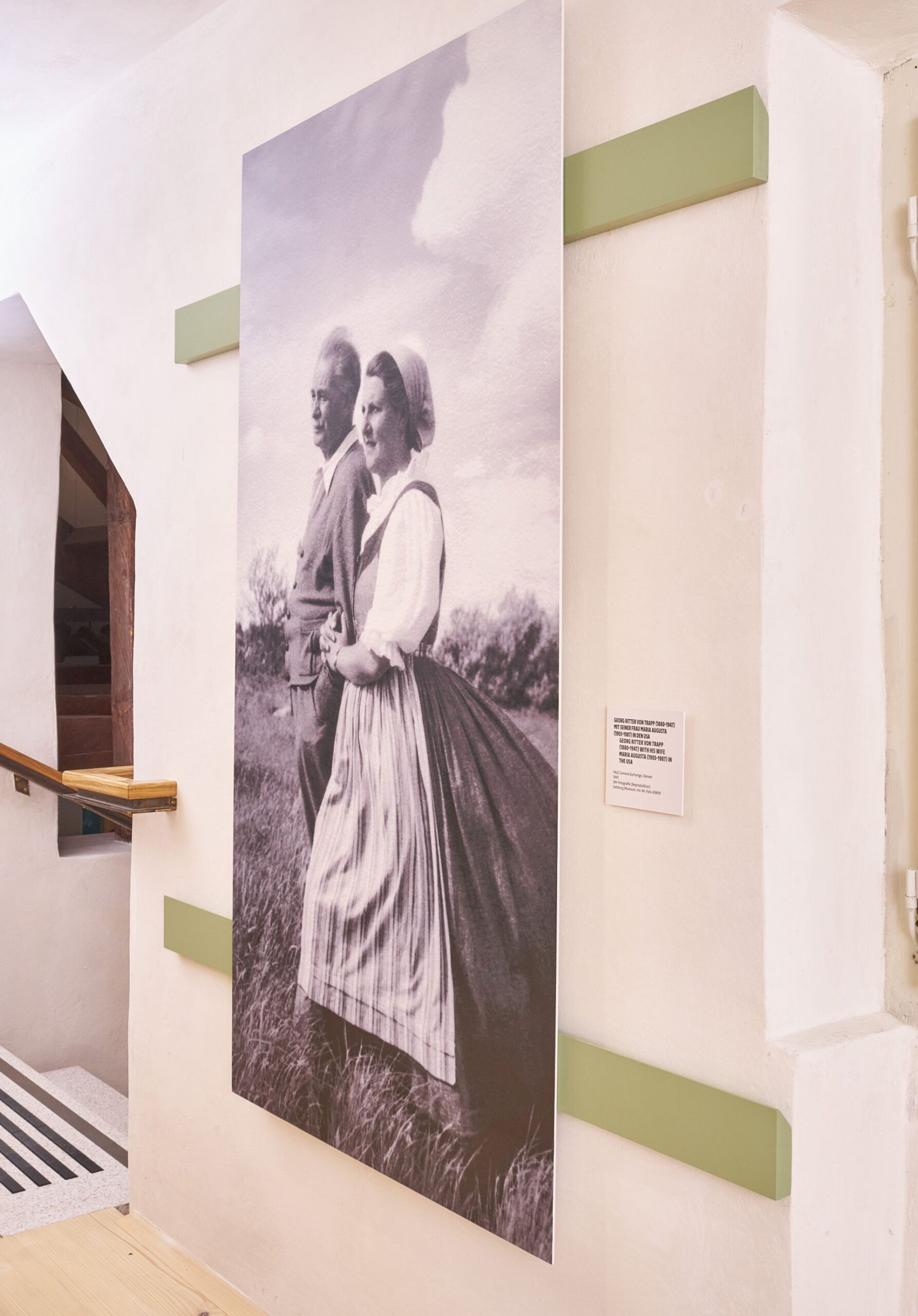 Gro&szlig;es Schwarz-Wei&szlig;-Foto eines Paares in traditioneller Tracht, das an einer Wand in einem hellen Flur h&auml;ngt.