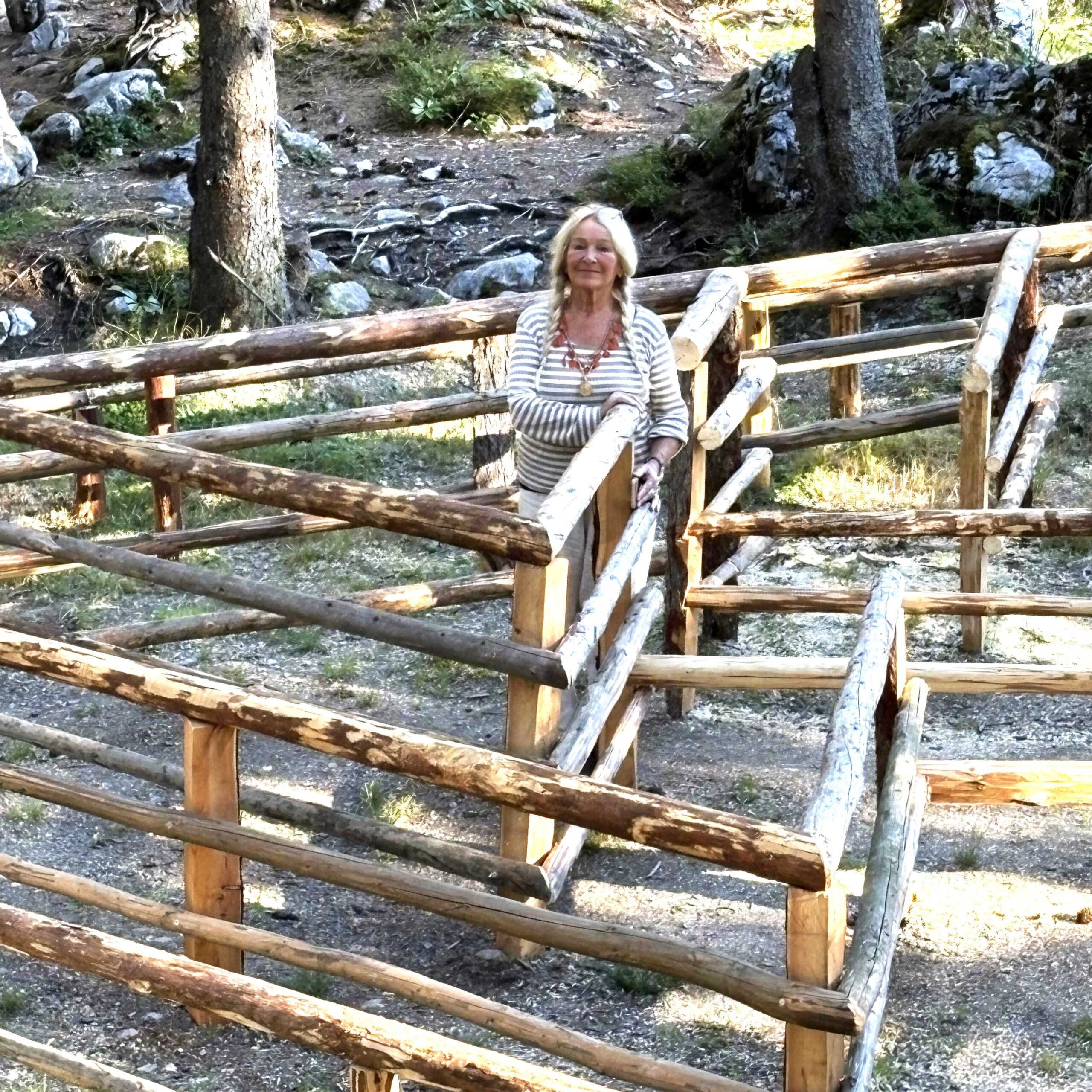 Eine Frau steht auf einem labyrinthartigen Holzpfad in einem sonnenbeschienenen Wald, der Teil eines einzigartigen Bergkunstprojekts ist.