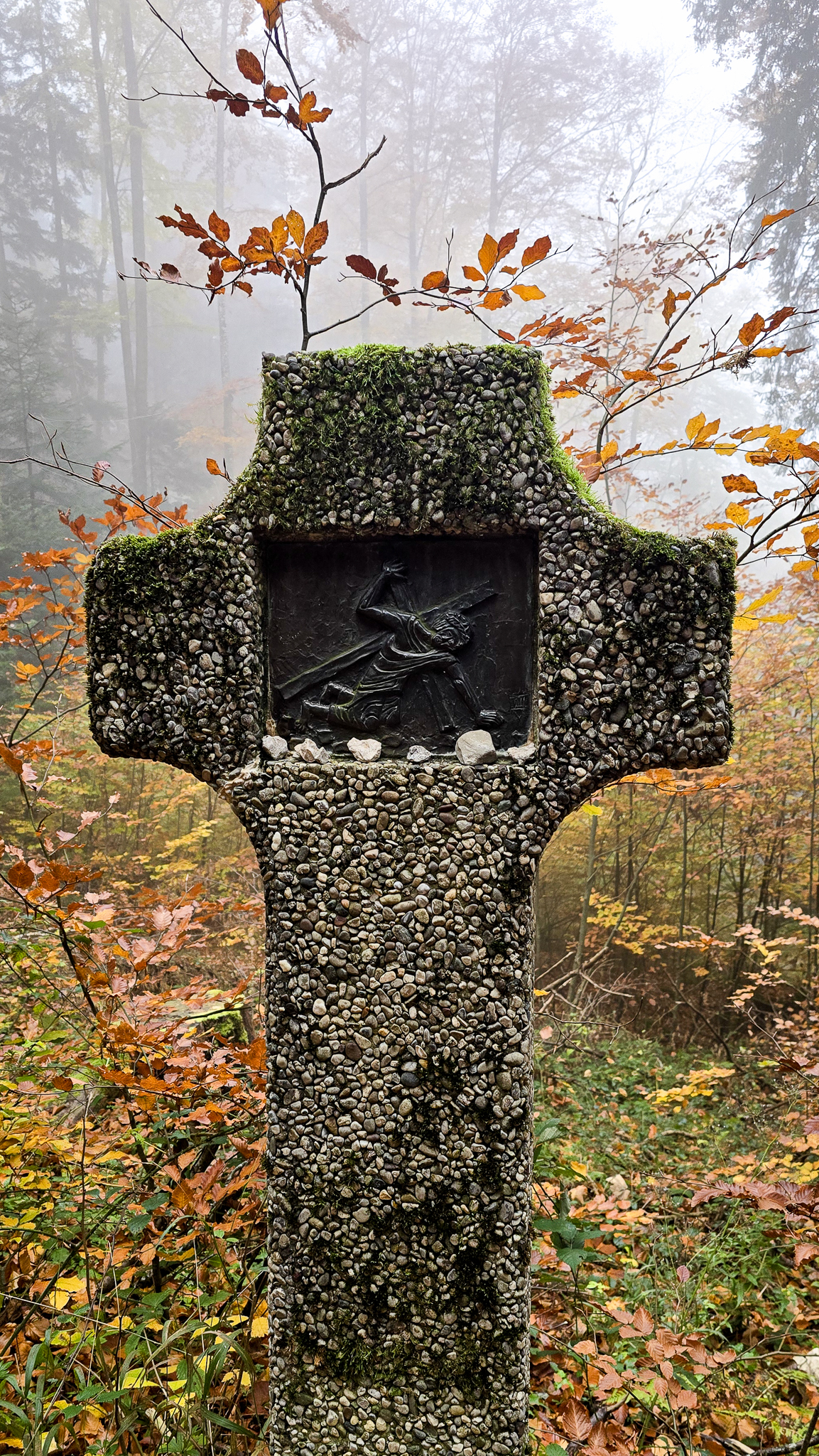 Steinkreuz mit Relief und Moos; Herbstb&auml;ume und Nebel lassen den Geist des Wolfgangi-Kirtags aufleben.