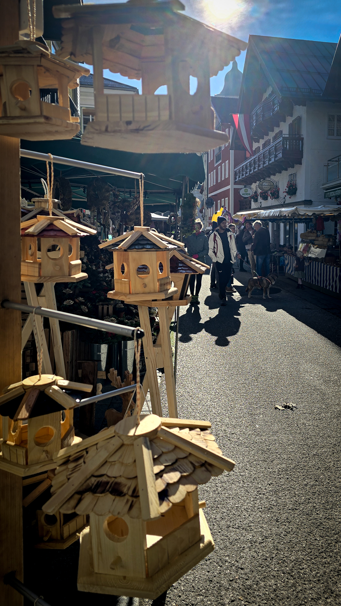 Holzvogelh&auml;uschen, die auf dem Wolfgangi Kirtag zum Verkauf stehen &ndash; einem sonnigen &ouml;sterreichischen Markt, auf dem es vor Menschen und Geb&auml;uden nur so wimmelt.