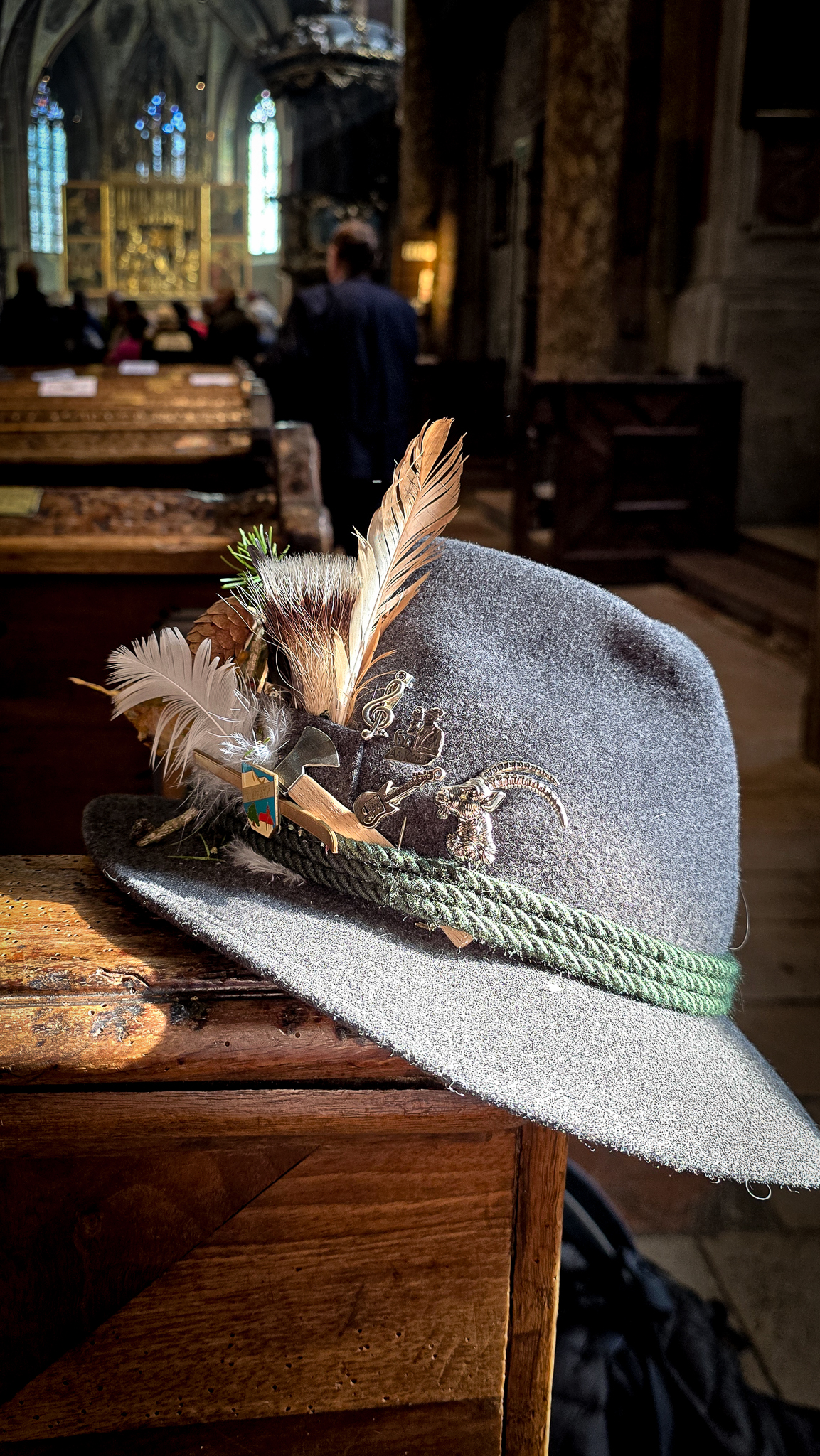 Ein grauer Filzhut mit Federn und Anstecknadeln liegt auf einem St&uuml;ck Holz in einer Kirche beim Wolfgangi-Kirtag.