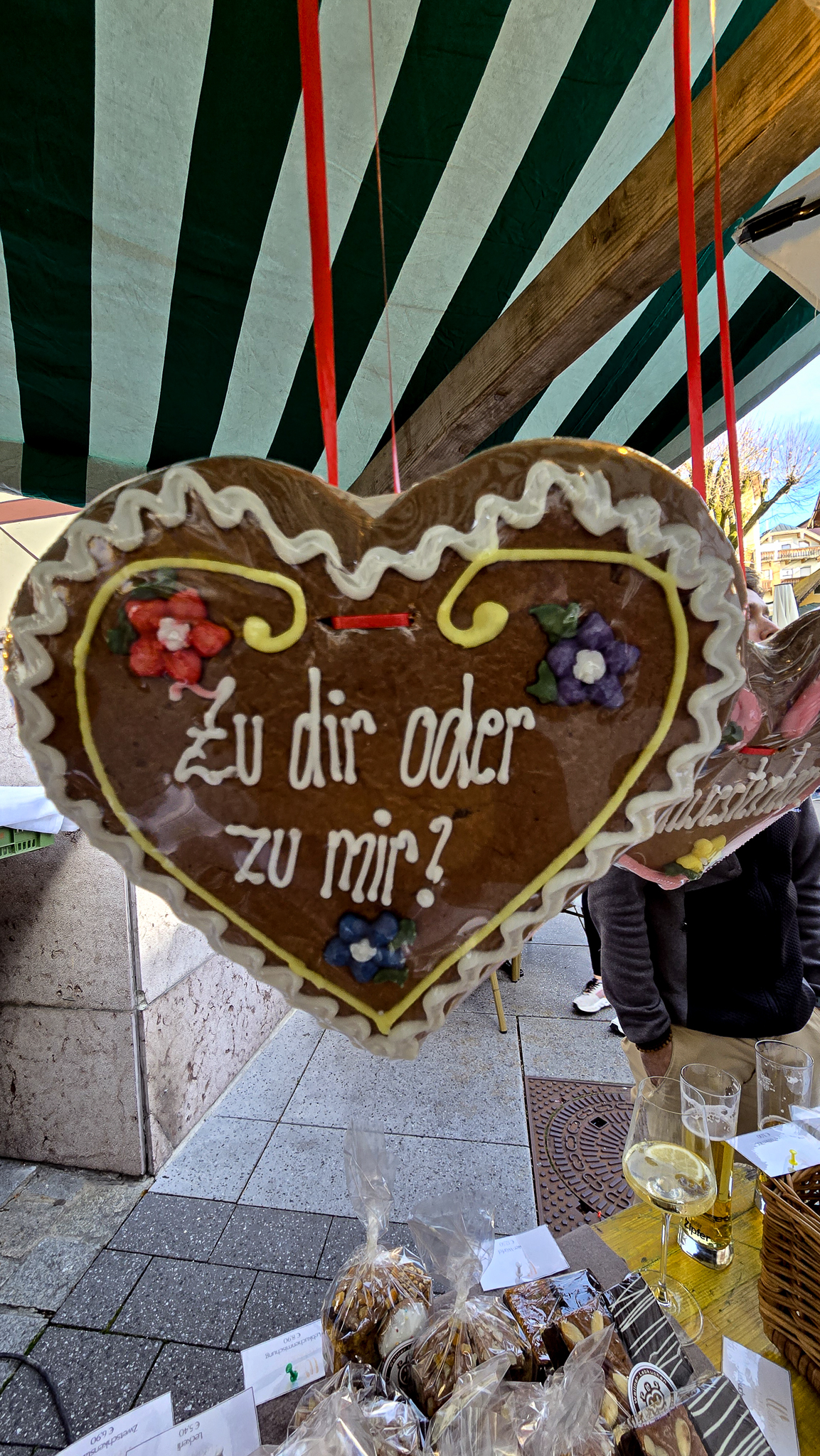 Herzf&ouml;rmiger Lebkuchen mit deutscher Aufschrift auf dem Wolfgangi-Kirtag-Flohmarkt, dar&uuml;ber ein gestreiftes Vordach.
