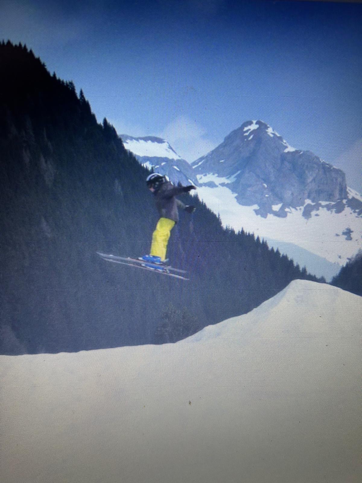 Ein Skifahrer in gelben Hosen springt in den Bergen von einer Rampe.
