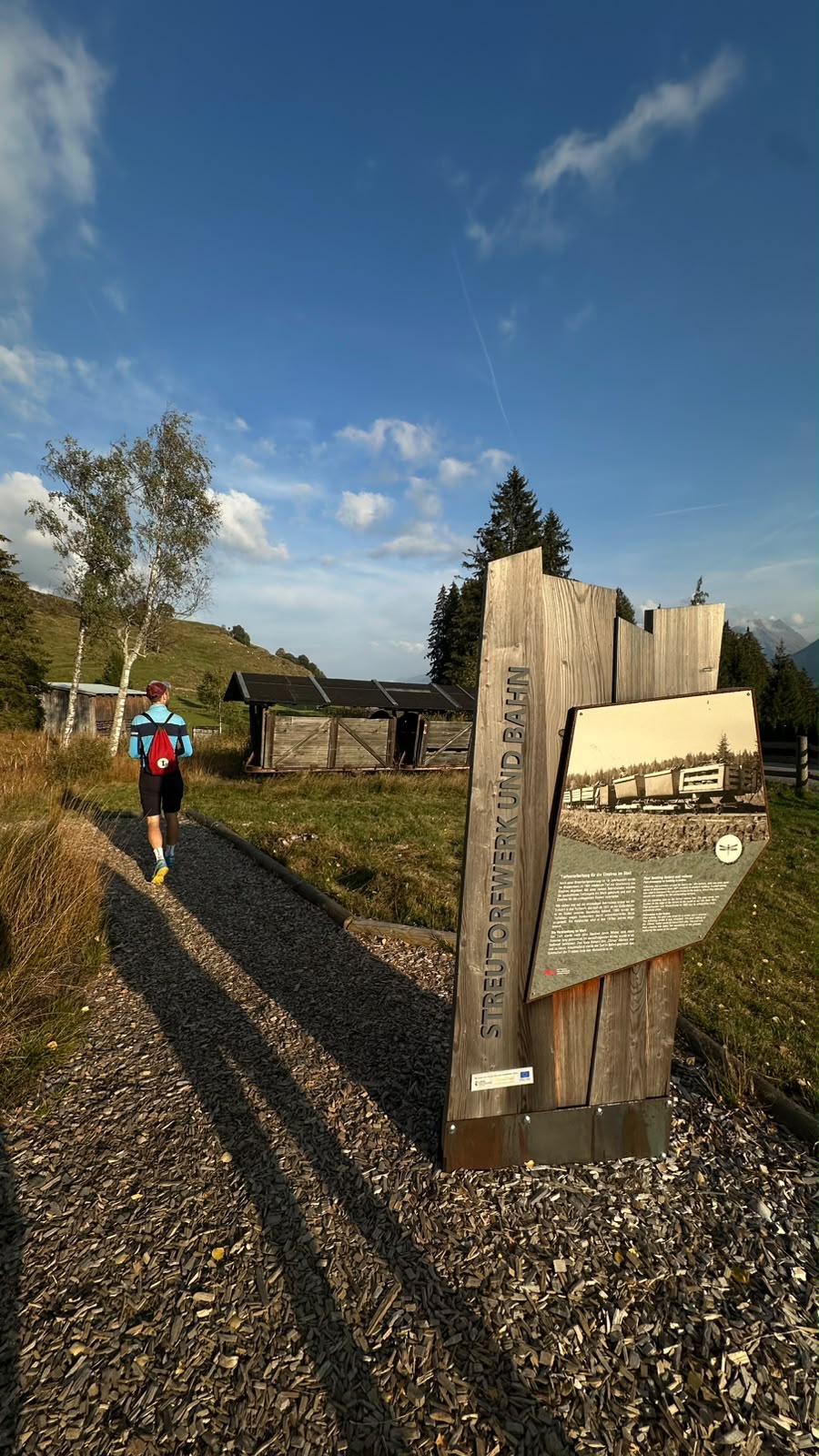 Ein Wanderer, der auf einem Schotterweg an einer Informationstafel über das Streutorfwerk und die Bahn vorbeigeht.