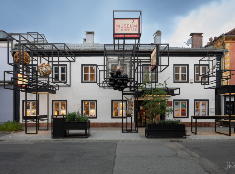 Das Museum Fronfeste befindet sich in einem weißen Gebäude mit schwarzer Stahlkonstruktion, skulpturalen Akzenten und Pflanzkübeln am Gehweg.