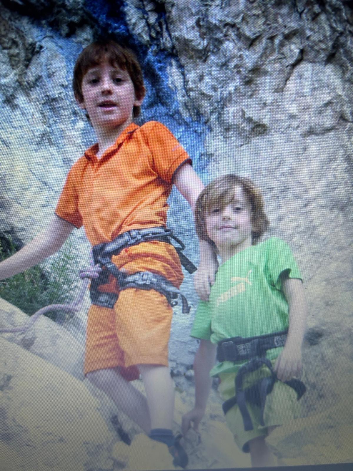 Zwei Jungen in Klettergurten stehen auf einem felsigen Bergpfad.