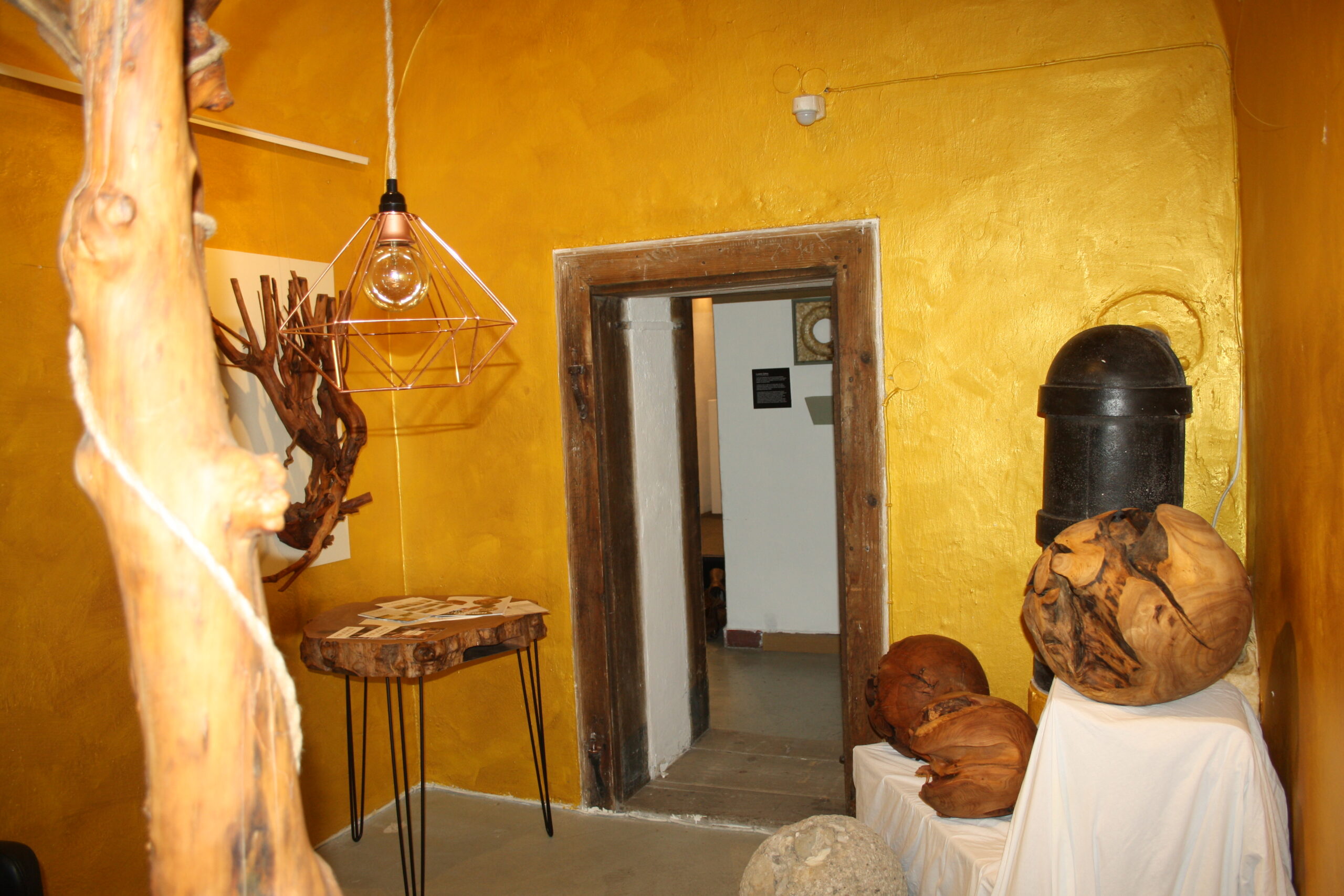 Ein Raum mit goldenen Wänden, einer Pendelleuchte aus Draht und skulpturalen Dekorelementen aus Holz.