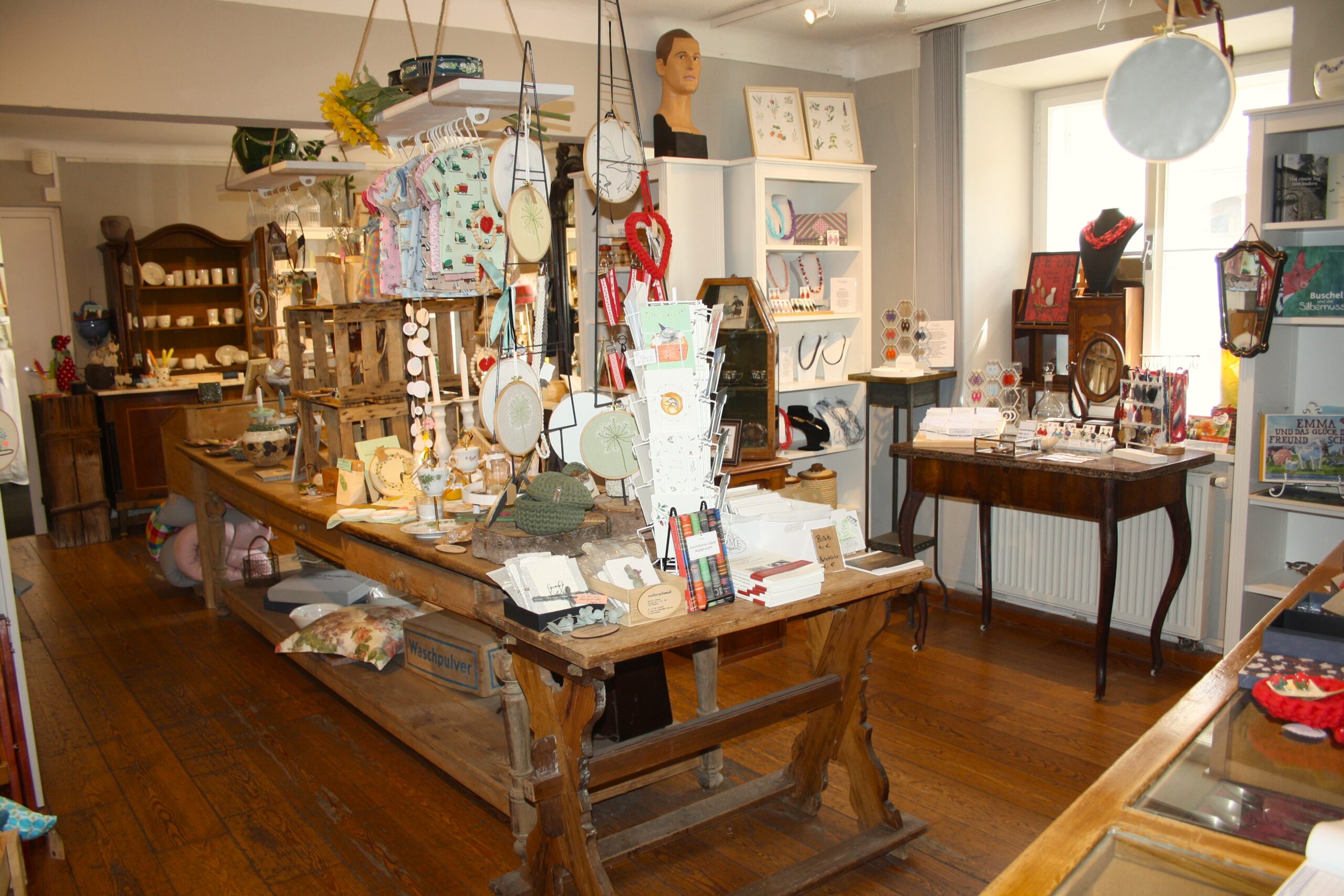 Innenansicht eines Souvenirladens, in dem auf Ausstellungs- und Regaltischen verschiedene Wohnaccessoires, Schmuck und Kinderkleidung ausgestellt sind.