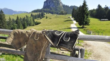 Zwei Lederhosen hängen über einem Zaun bei einer Almhütte